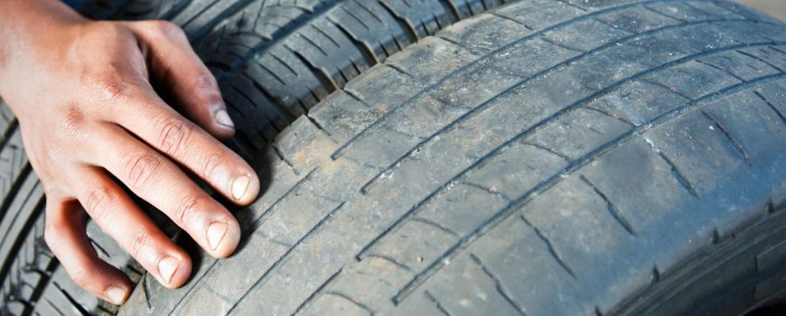 Mano encima de dos neumáticos, uno con el dibujo más completo y otro más desgastado
